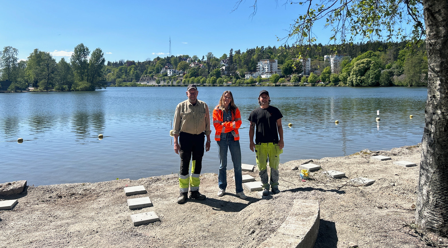 Alice Fredriksson, projektledare, tillsammans med snickarna som jobbar med bryggan på Mossberget, med vattnet i bakgrundn.