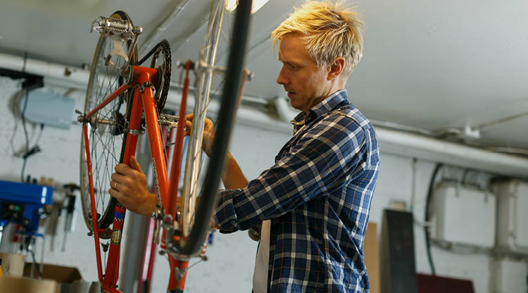Man som står i en verkstad och lagar sin cykel. 