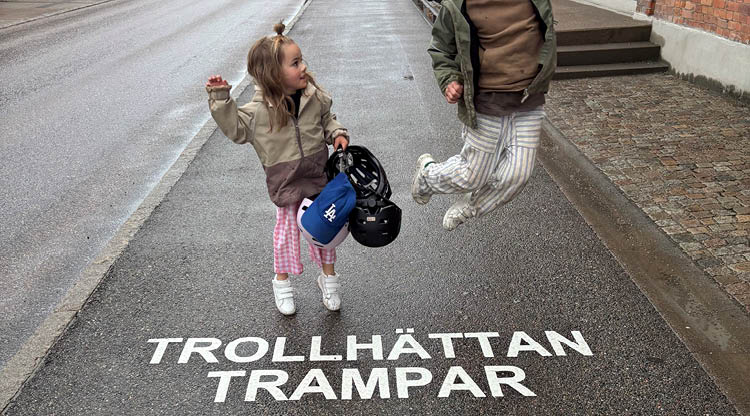 Två barn står vid texten ”Trollhättan trampar” som är målad på gatan.