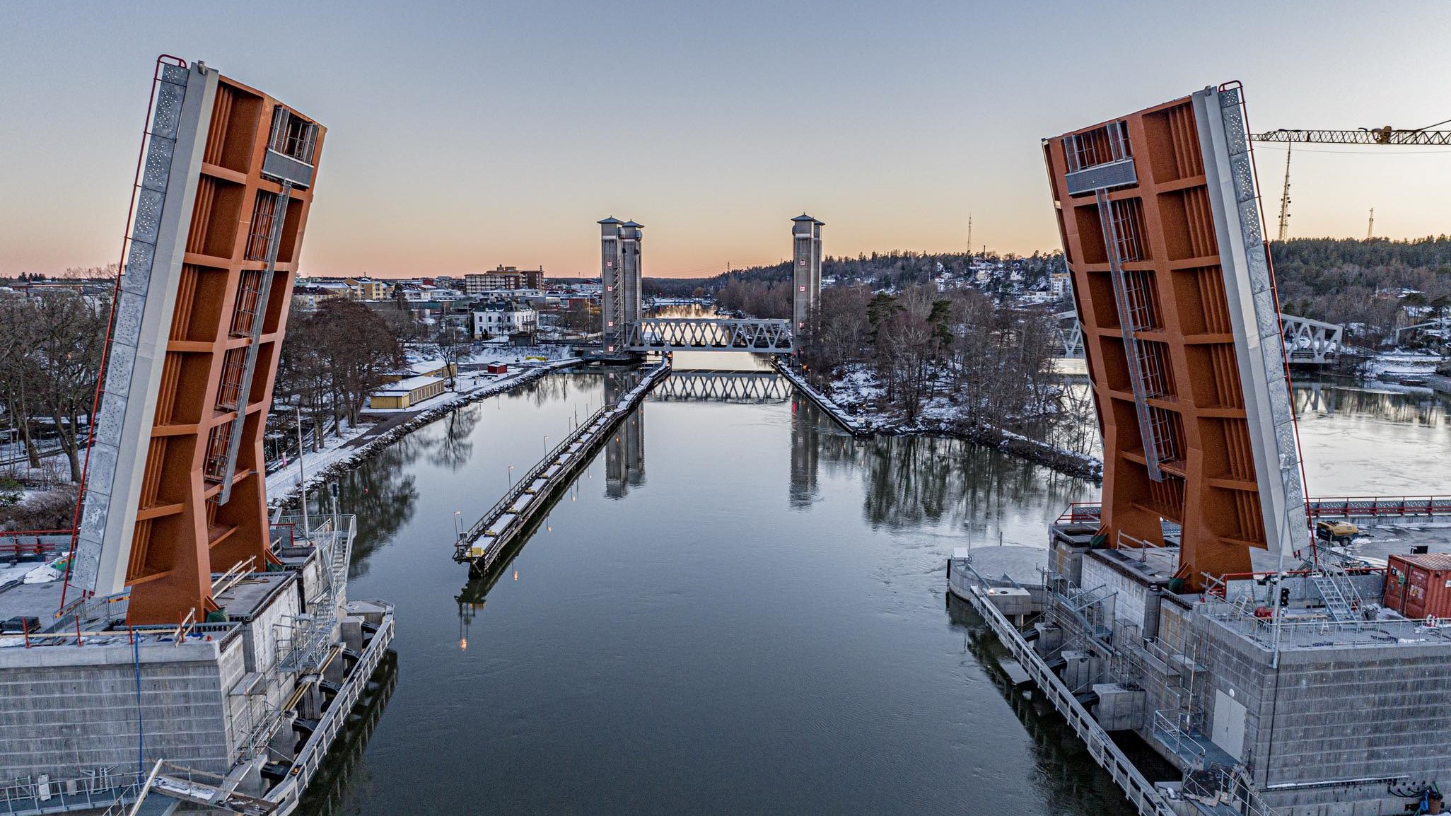 En stor klaffbro med uppfällda klaffar i förgrunden, över en älv. Längs älvsidorna finns flerbostadshus och stadsmiljö, i bakgrunden finns ytterligare en bro och berg.