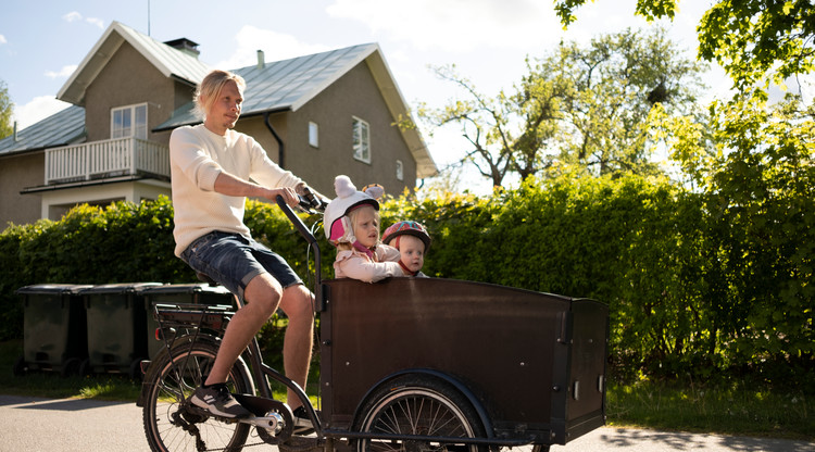 Man som cyklar med två barn i lådcykel