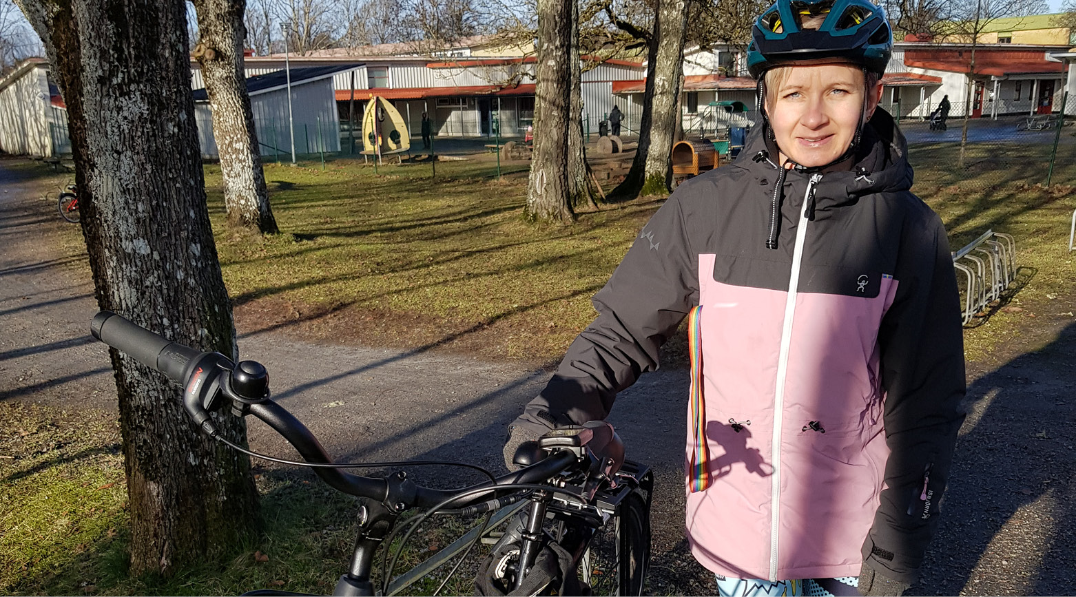 Bild på en kvinna med cykelhjälm som står bredvid en svart cykel.