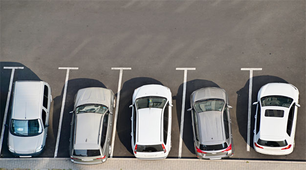 Foto taget ovanifrån på en asfalterad parkering, fem bilar står parkerad på rad.