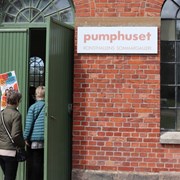 Personer går in i byggnad där det är en skylt där det står pumpahuset.