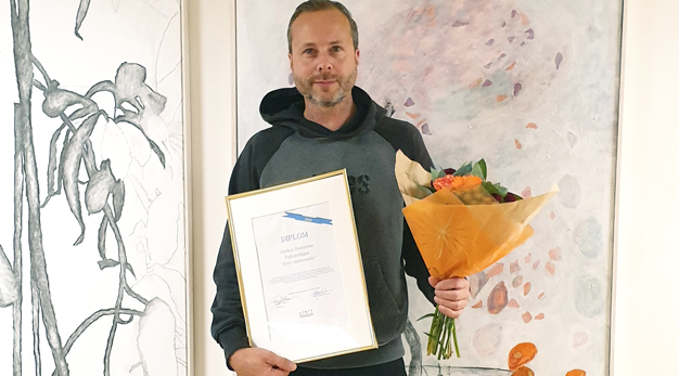 Marcus Rudström håller i ett diplom och blombukett. Han ser glad ut.