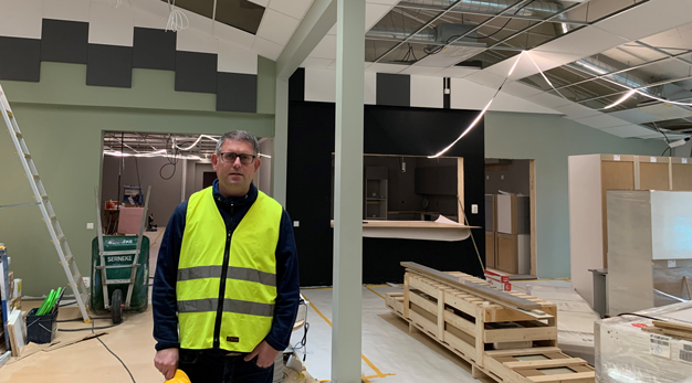 En man inklädd reflexväst och med en bygghjälm i handen står i en lokal under byggnation.