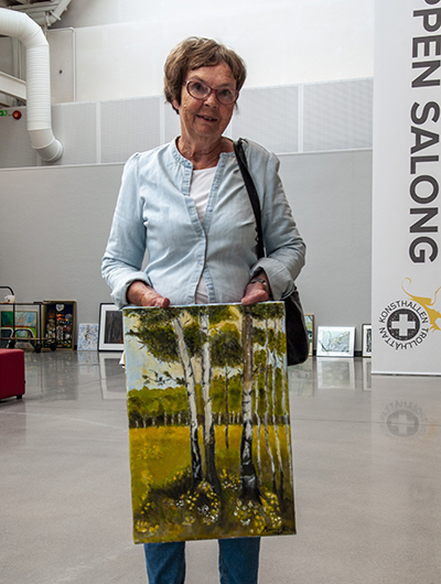 En kvinna håller upp sitt bidrag till Öppen salong 2020, en tavla på tolkning av temat skog.