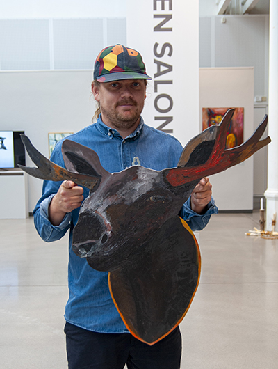 En man håller upp sitt bidrag till Öppen salong 2020, en tavla som tolkar temat skog.