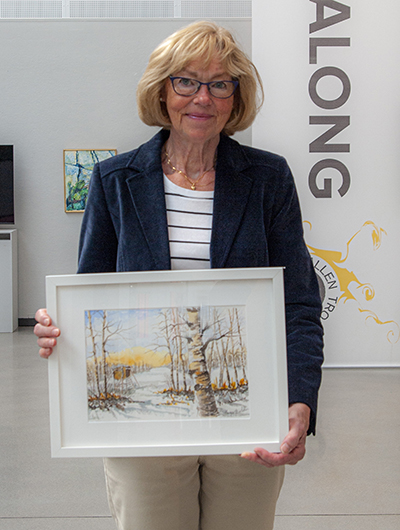 En kvinna håller upp sitt bidrag till Öppen salong 2020, en tavla som tolkar temat skog.
