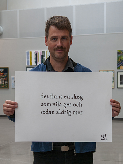 En man håller upp sitt bidrag till Öppen salong 2020, en tavla som tolkar temat skog.