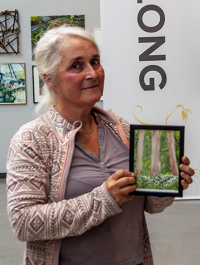 En kvinna håller upp sitt bidrag till Öppen salong 2020, en tavla som tolkar temat skog.