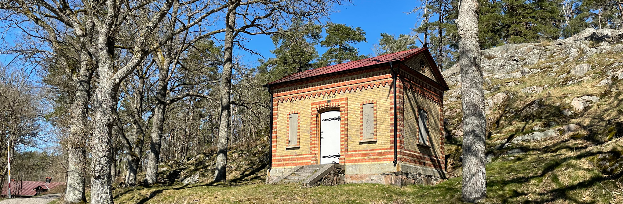Gammal arkivbyggnad i tegel i en skogsdunge.