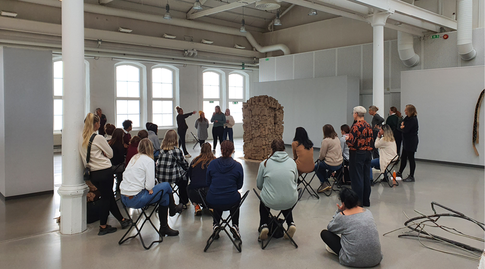 Personer samlade i en konsthall och lyssnar på någon som berättar om konsten.