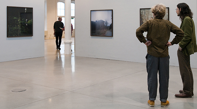 Två personer betraktar fotografier i en konsthall