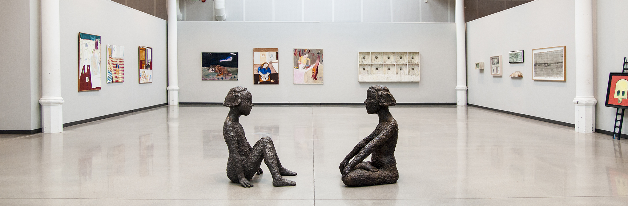 Två skultpturer, flickgestalter, sitter vända mot varandra. 