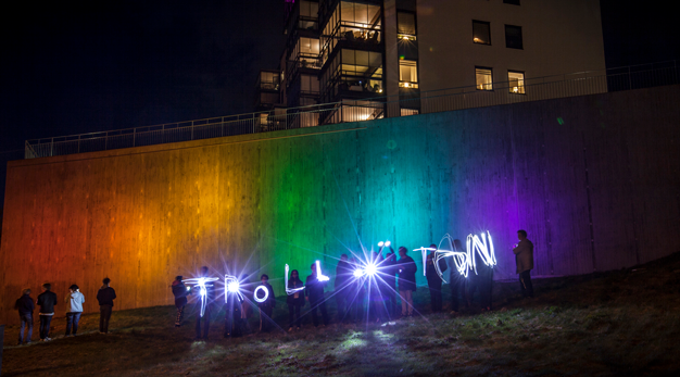 Ungdomar skriver Trollhättan med ficklampor mot en betongvägg ljussatt i olika färger