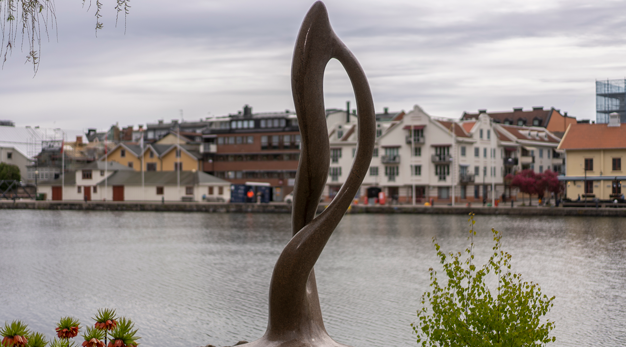 En stor stenskulptur med vatten och hus i bakgrunden.