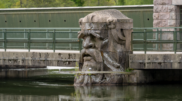 Manligt stenhuvud med mustasch på en stenbro. 