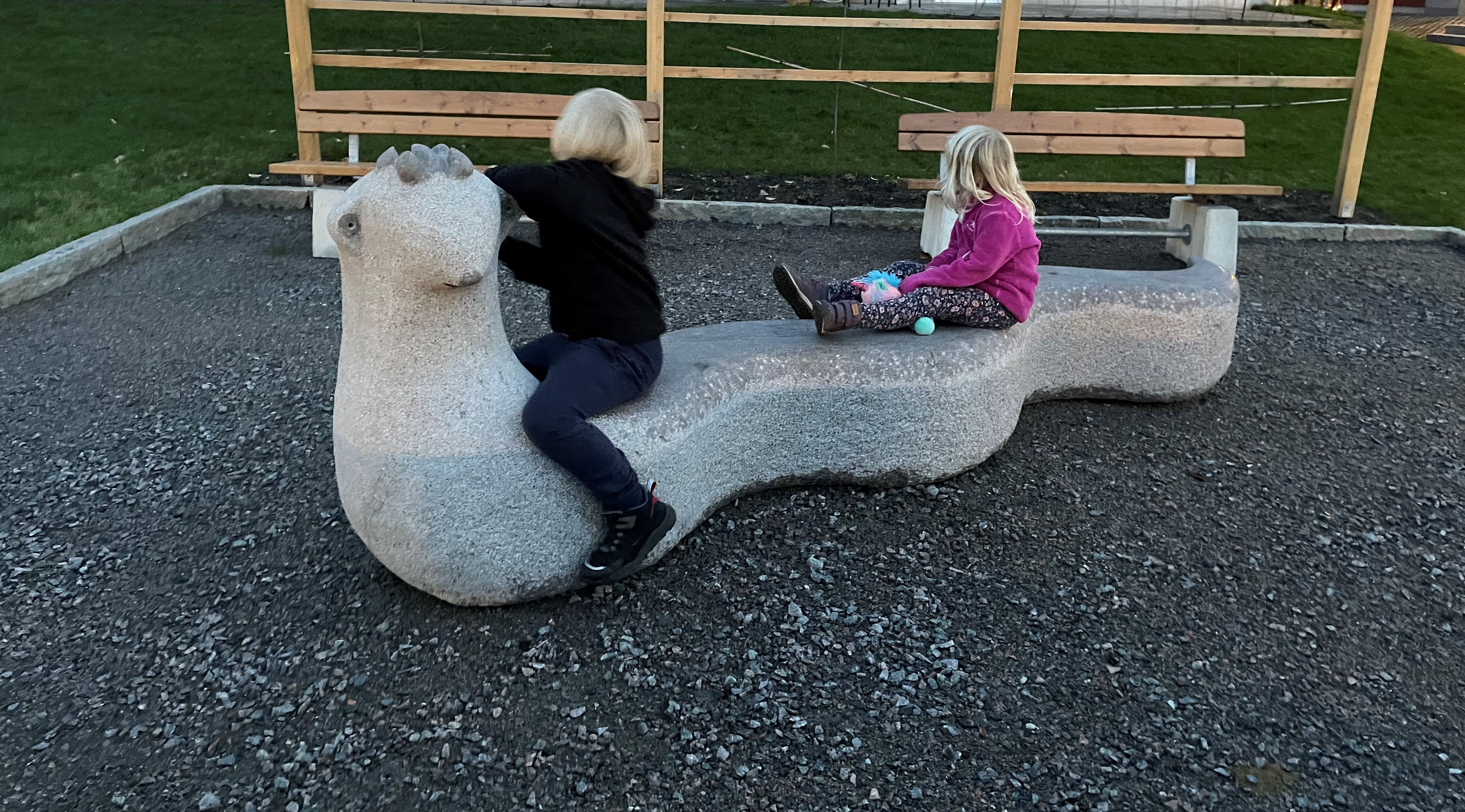 Två barn sitter på en låg maskformad skulptur 