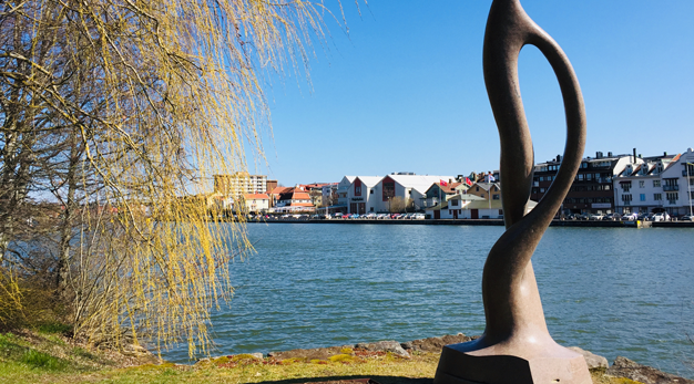 En stor stenskulptur med vatten och hus i bakgrunden.