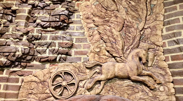 Relief på tegelvägg som avbildar en häst som drar en vagn. 