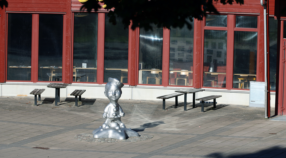 Skulptur i aluminium föreställande en pojke med skepparmössa står på en stor sjöstjärna framför Kronan Kulturhus