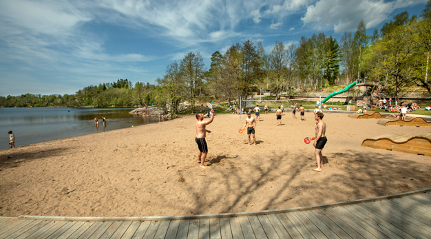 En strand där killar spelar beachtennis och barn som vadar i vattnet