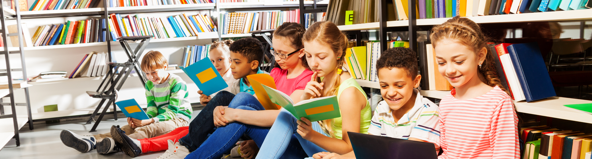 Barn sitter på golvet i ett bibliotek och läser