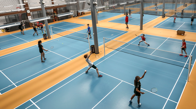 Barn spelar badminton inomhus i en badmintonhall.