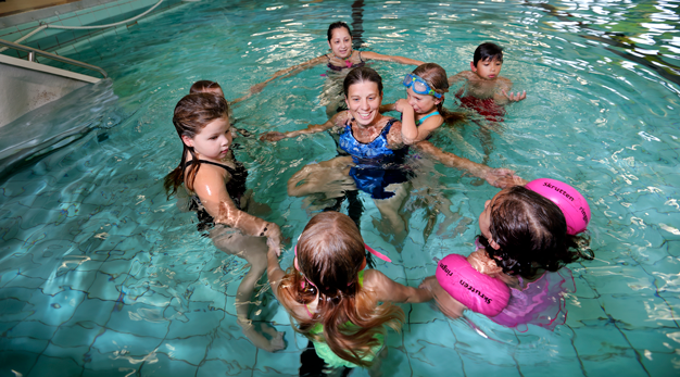 Barn samlade i en ring runt simläraren i bassängen. 
