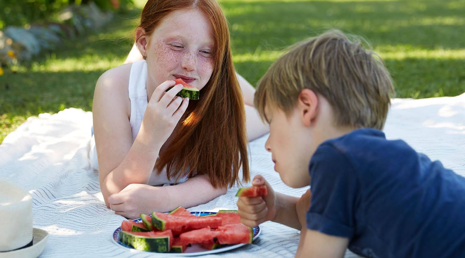 Två barn som äter vattenmelon på filt på gräsmatta