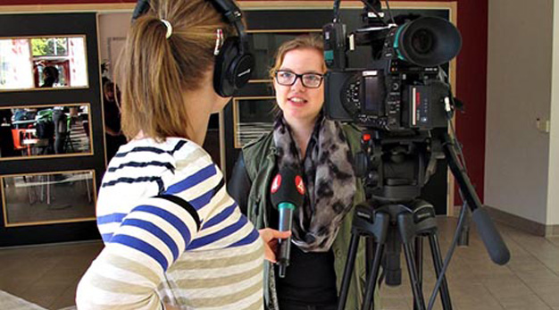 En tjej i högstadiet blir intervjuda av en reporter från TV4. Man ser ryggen på reportern och videokameran, hon håller upp en mikrofon med TV4 logotypen på. 