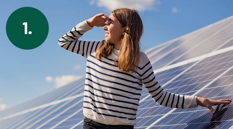 Tjej som står vid solcellspark och tittar upp mot solen.