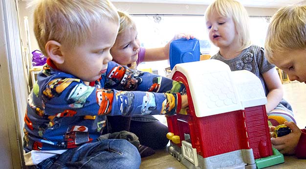 Fyra barn som sitter på golvet och leker med ett leksakshus