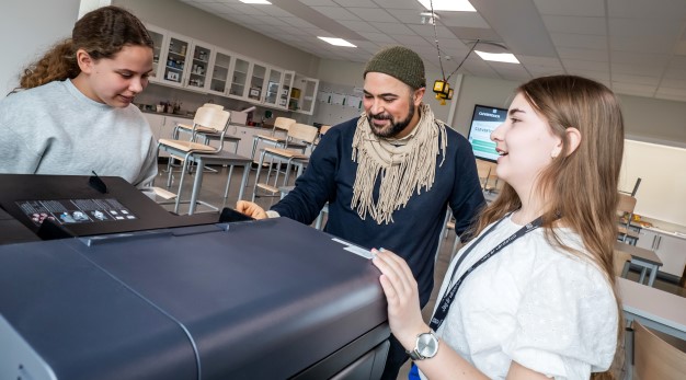 Ett klassrum med många elever. En elev räcker upp handen