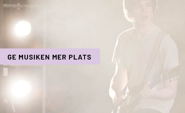 Kille som spelar elgitarr på scen med scenljus lysande bakifrån. 