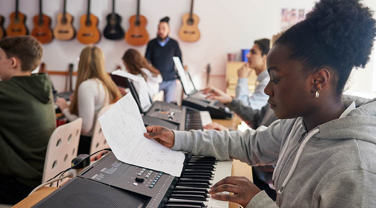 Tjej som spelar piano, resten av klassen i bakgrunden och en vägg med gitarrer. 