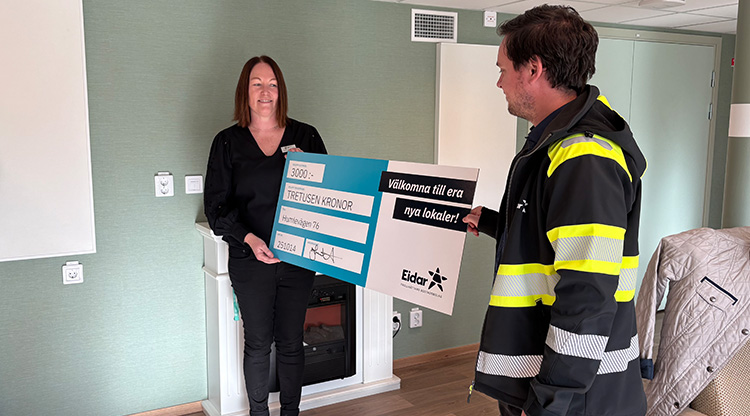 Kvinna håller i en stor check. En man står på andra sidan.
