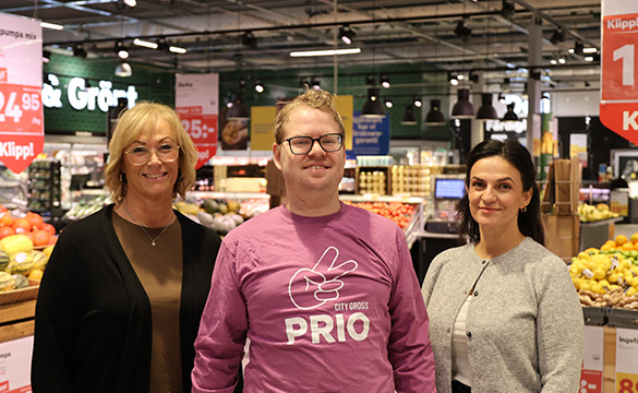 Tre personer ler och tittar in i kameran. Står i en mataffär. Foto.