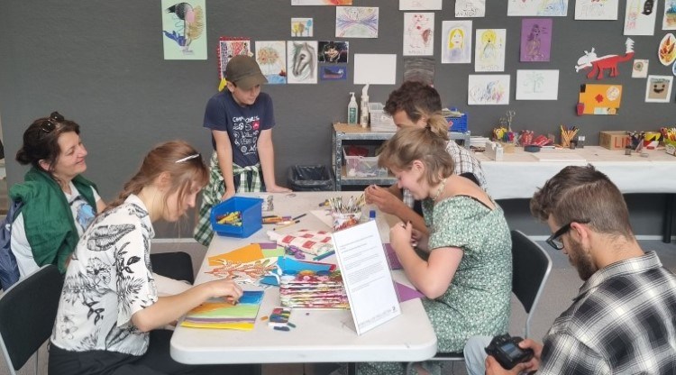 Familj som sitter och skapar vid ett bord i konsthallens öppna ateljé