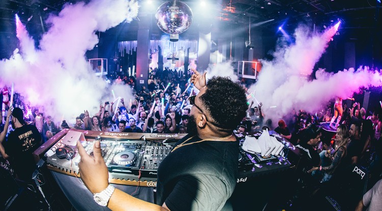 DJ spelar på en klubb där publikhavet dansar på ett rökfyllt dansgolv